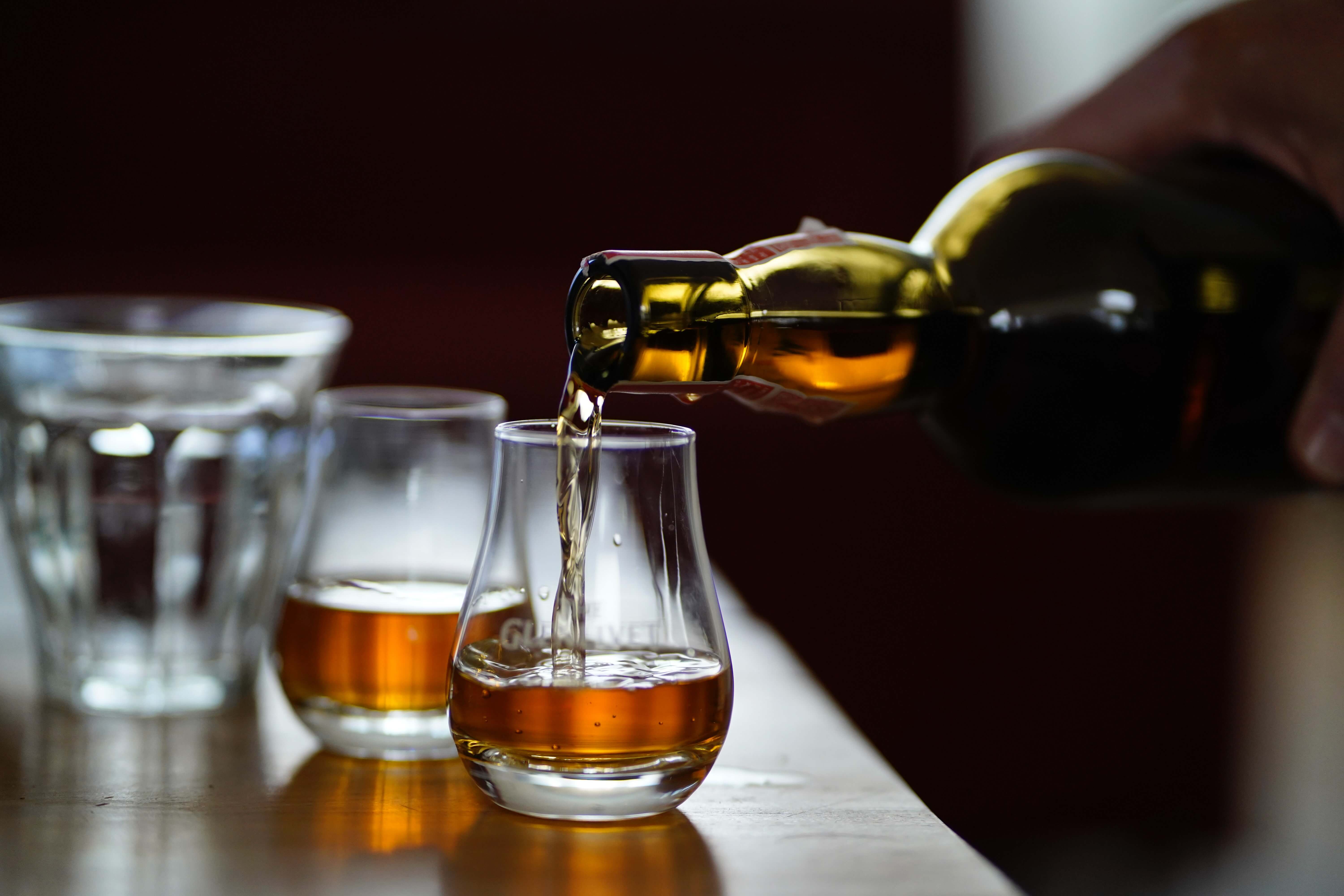 Hand holding whiskey bottle and pouring into glass